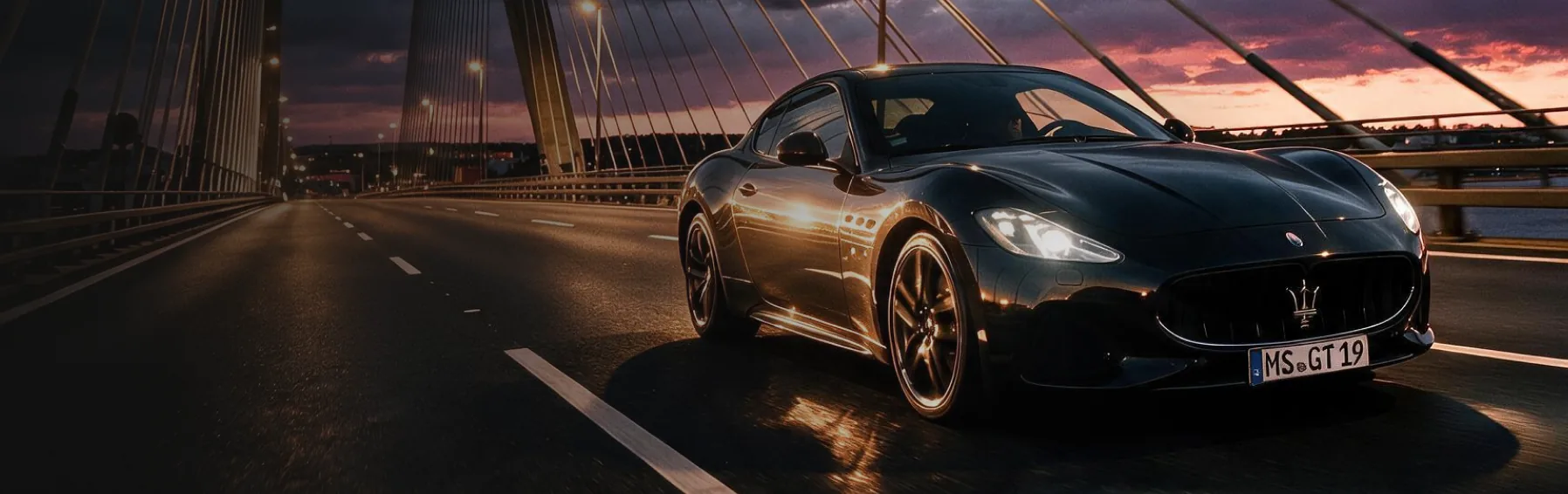 Black sports car crossing a cable-stayed bridge at sunset